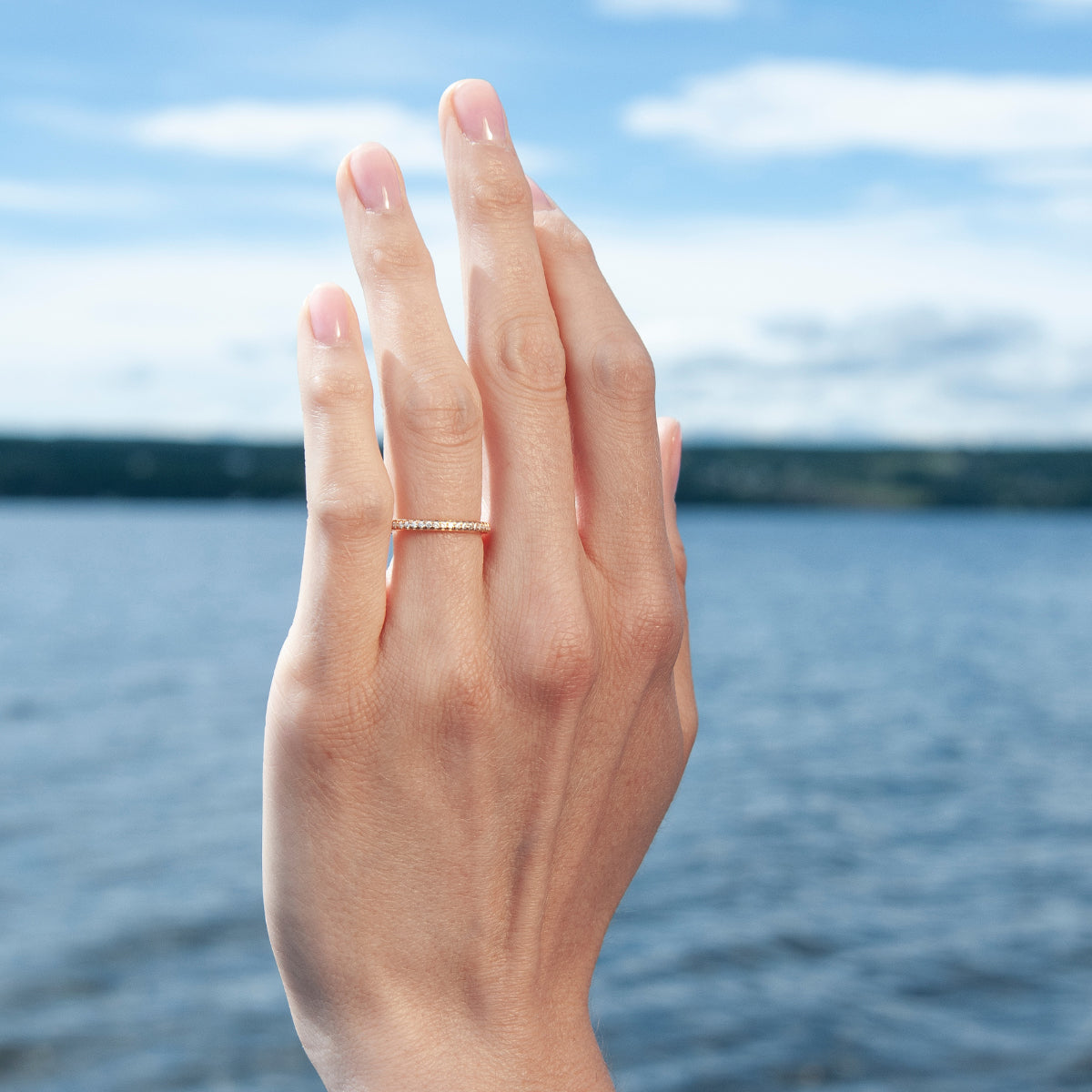 Alliansring i guld från Aure med små diamanter, buren på hand framför vatten.