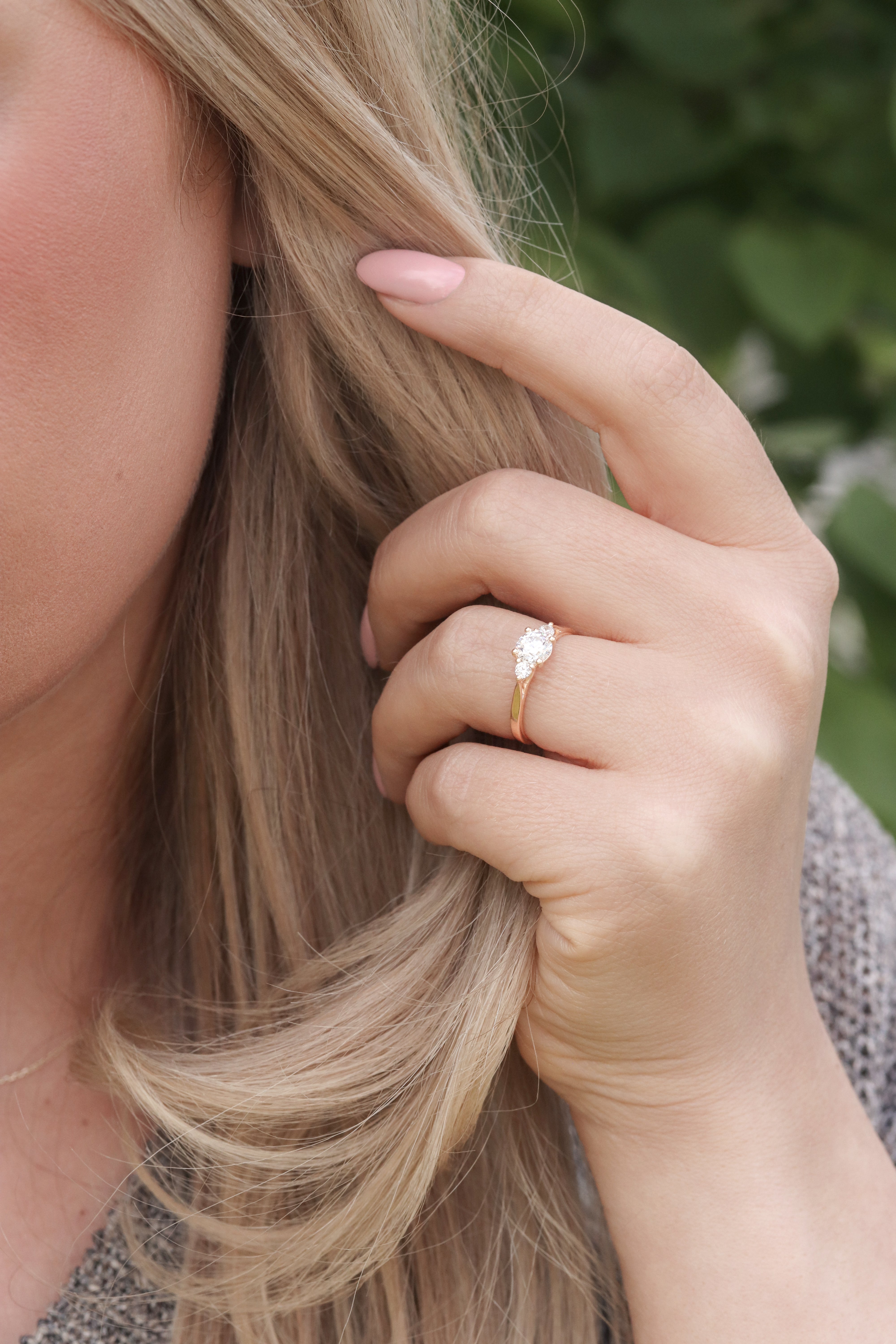 Eterna solitärring i rödguld med briljantslipad diamant buren på hand framför ljust hår.