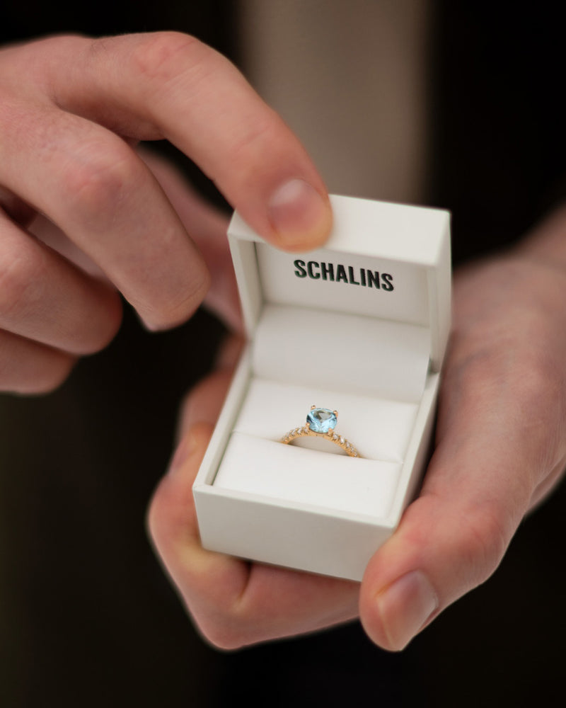 Hand håller öppen ringask från Schalins med ädelstensring i akvamarin, inspirerad av Frida Sömskars förlovning