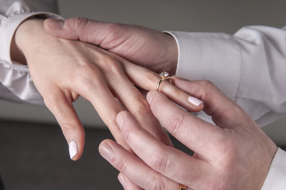 Bilden visar en manlig hand som trär på en förlovningsring på höger hand på en kvinnlig hand