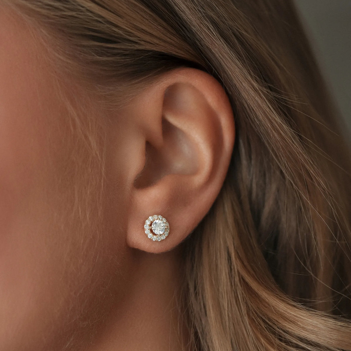 Närbild av ett öra med North Stud Halo från Schalins i rödguld med totalt 0,44 ct diamanter, med en rund mittdiamant omgiven av mindre diamanter.