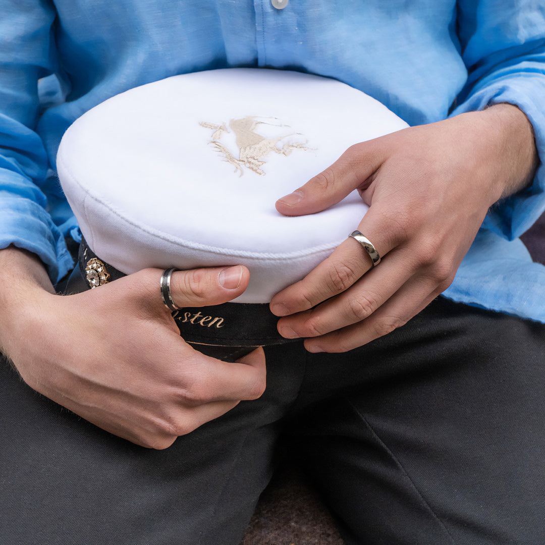 Studnet med studentmössa i knätt. Ringar på tumme och pekfinger. 