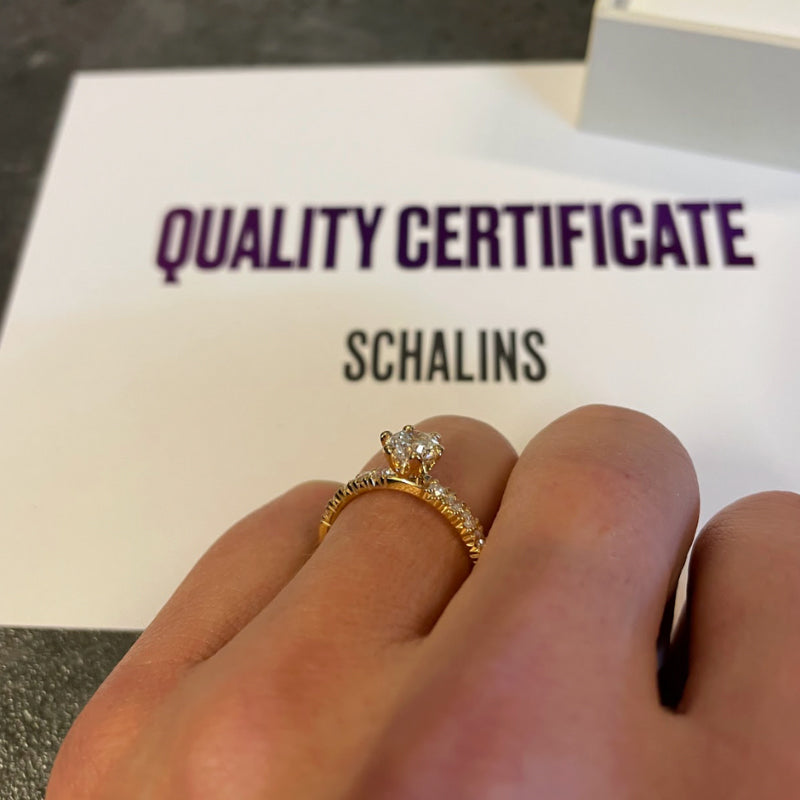 Hand som bär diamantring i guld framför Schalins quality certificate som visar äkthet och kvalitet