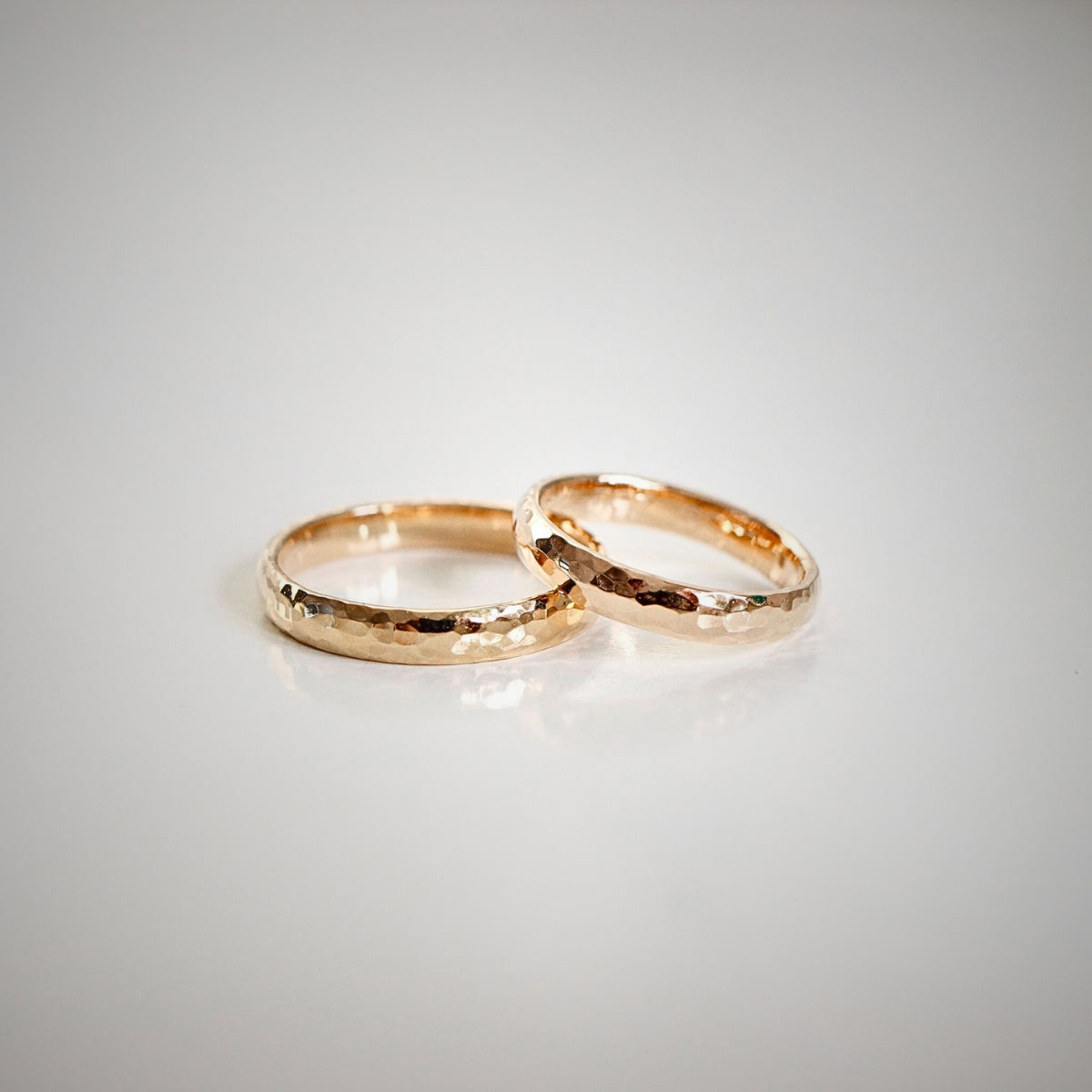 Två vigselringar i guld med hamrad och mönstrad yta på ljus bakgrund